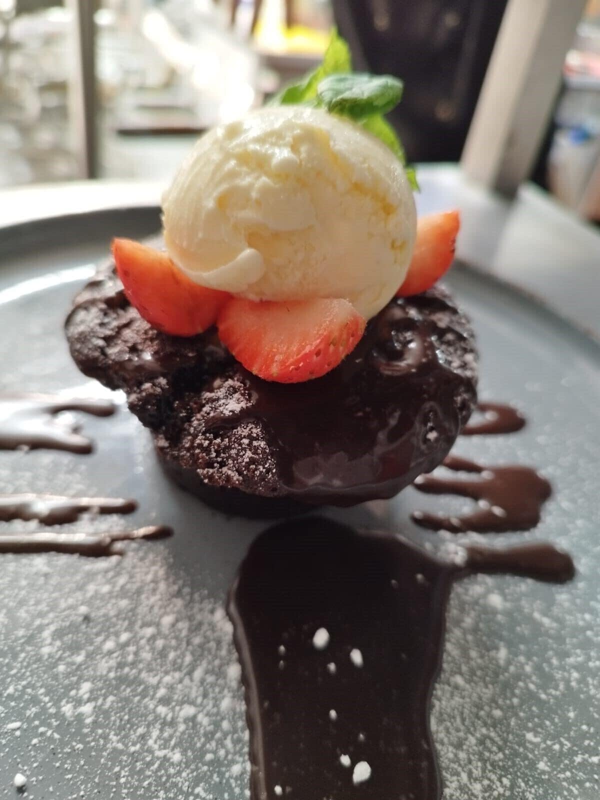 Postre con helado y fresas sobre una base de chocolate, servido en un plato con hilo de chocolate.