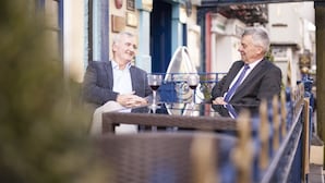 Two men seated at a table with wine glasses, in a setting with architectural details and a blue railing. - The Club House Hotel (Kilkenny)