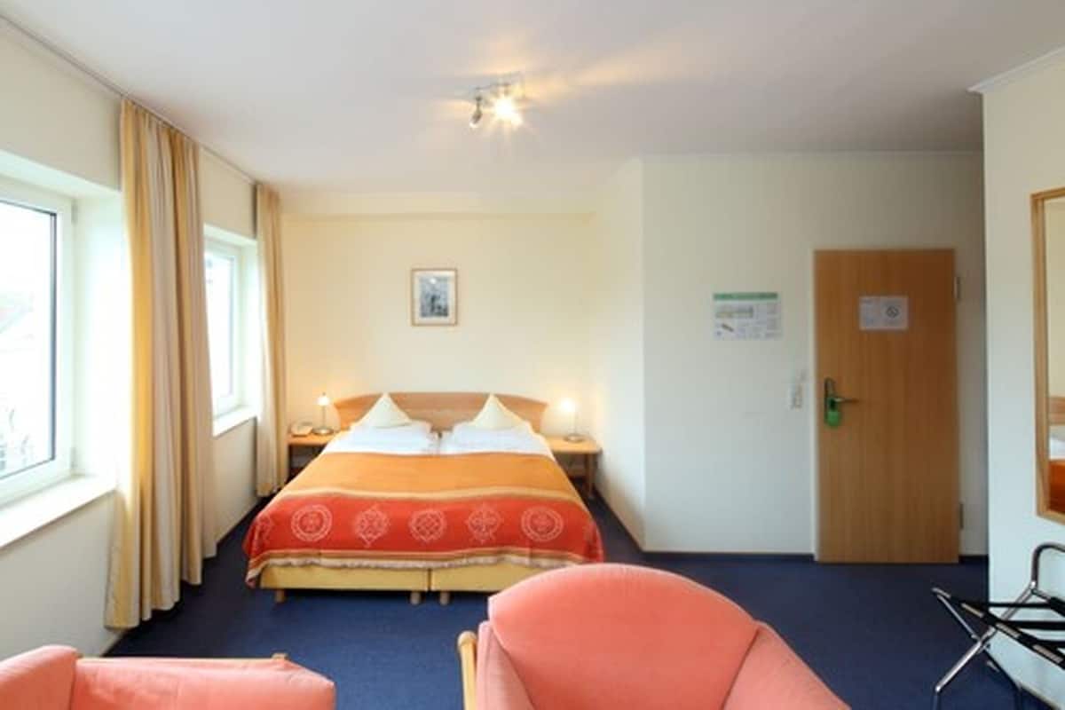 A hotel room with a bed, a nightstand, a chair, a door, and a window.