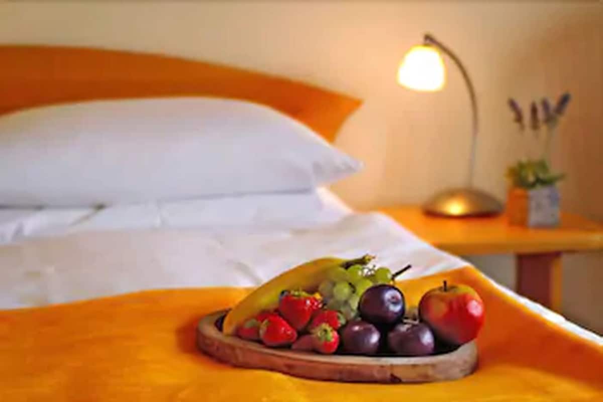 A bed with white linens and an orange headboard. A wooden tray with fruits is placed on the bed.