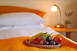 A bed with white linens and an orange headboard. A wooden tray with fruits is placed on the bed.