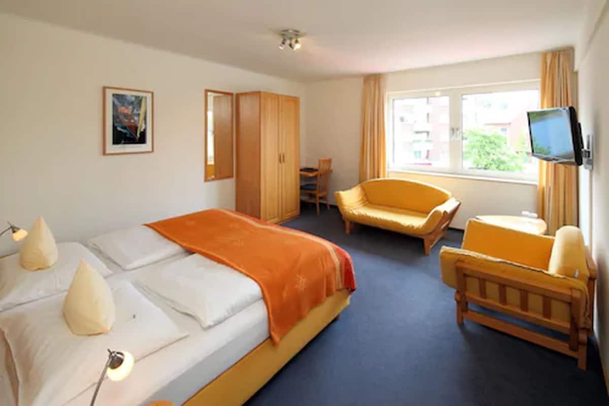 A hotel room with a bed, a chair, a desk, a television, and a wardrobe.