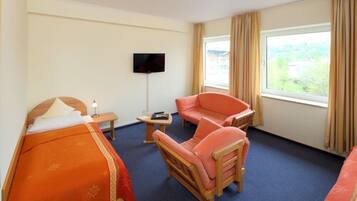 Een hotelkamer met een bed, een slaapbank, een stoel, een televisie en een raam met gordijnen.