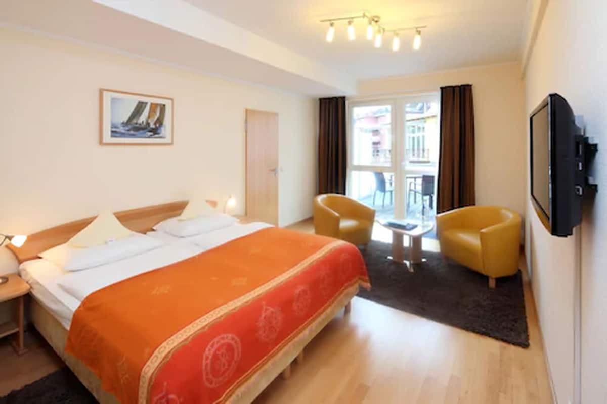A hotel room with a bed, two chairs, a TV, and a window with curtains.