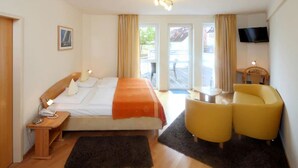 Habitación de hotel con cama, mesita de noche, lámpara y una pequeña mesa con sillas.