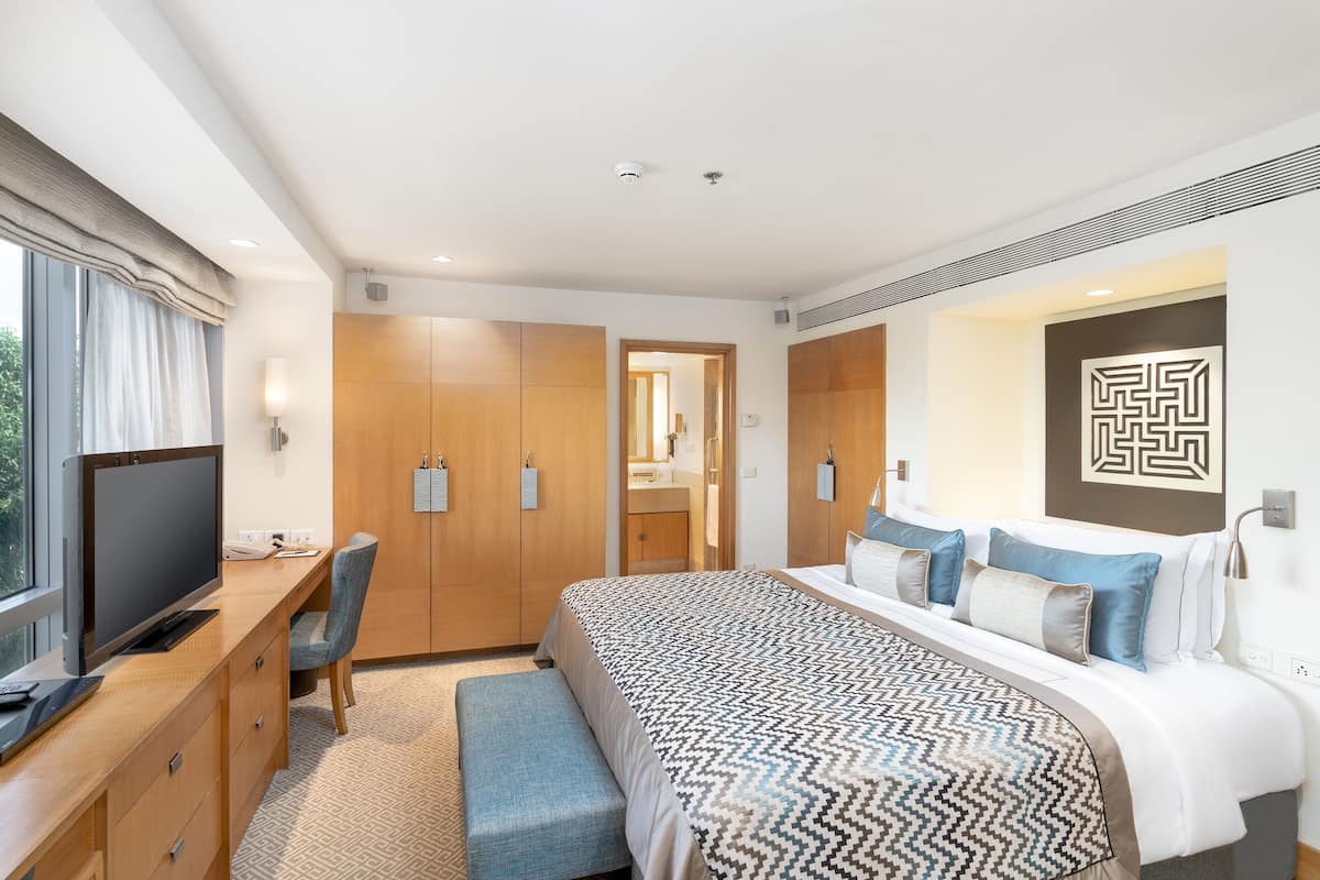 Una habitación de hotel moderna con una cama grande, un escritorio con televisión, una silla y un banco.