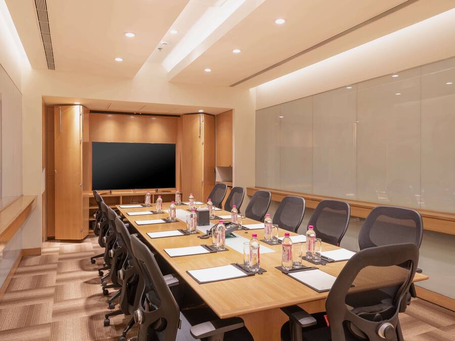A conference room with a long table, chairs, water bottles, and a projector screen.