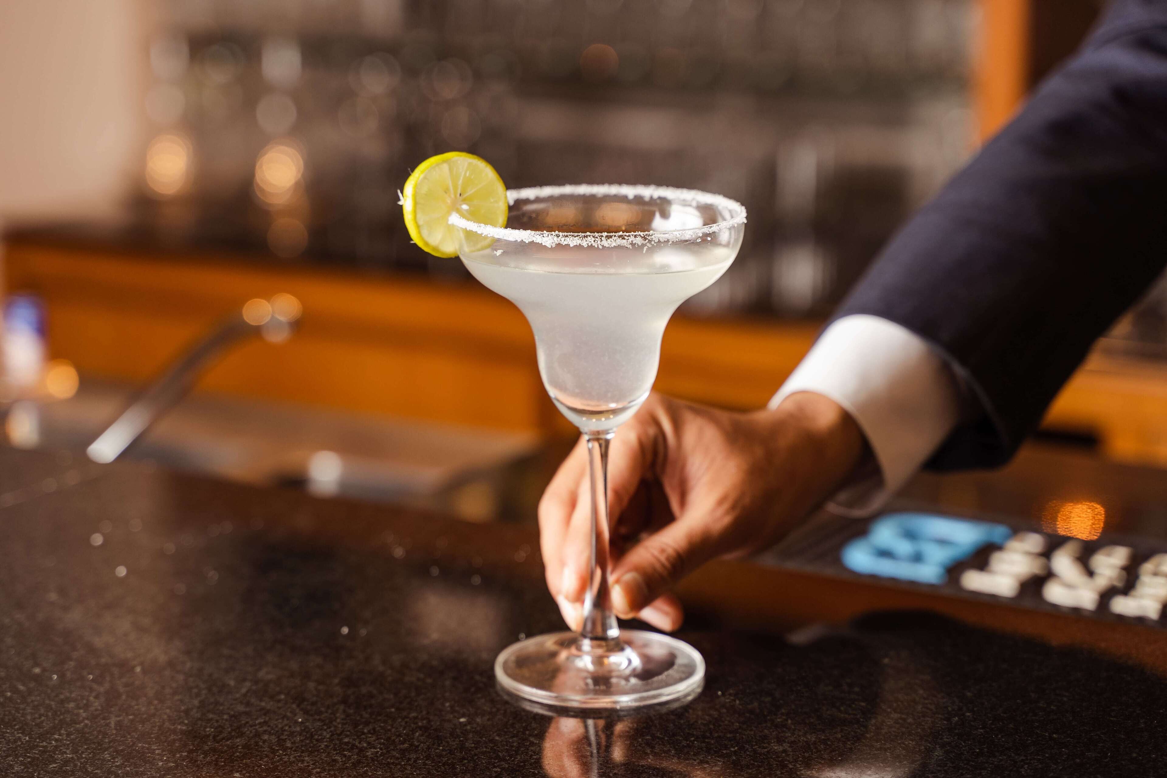 Een hand houdt een margarita glas vast, versierd met een limoen op een bargedeelte.