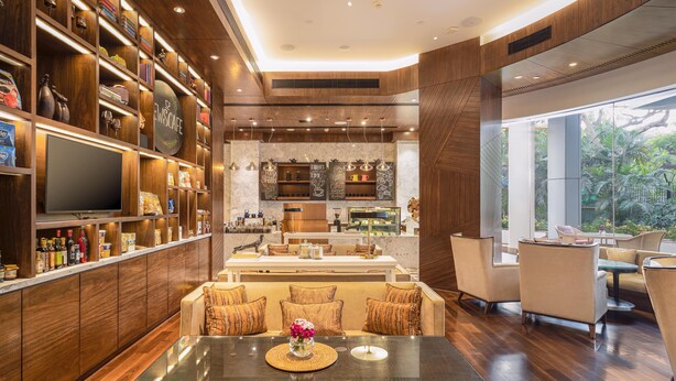 A modern bar area with wooden shelves, a flat-screen TV, and a seating area with a glass table. - Taj Wellington Mews Luxury Residences (Mumbai)