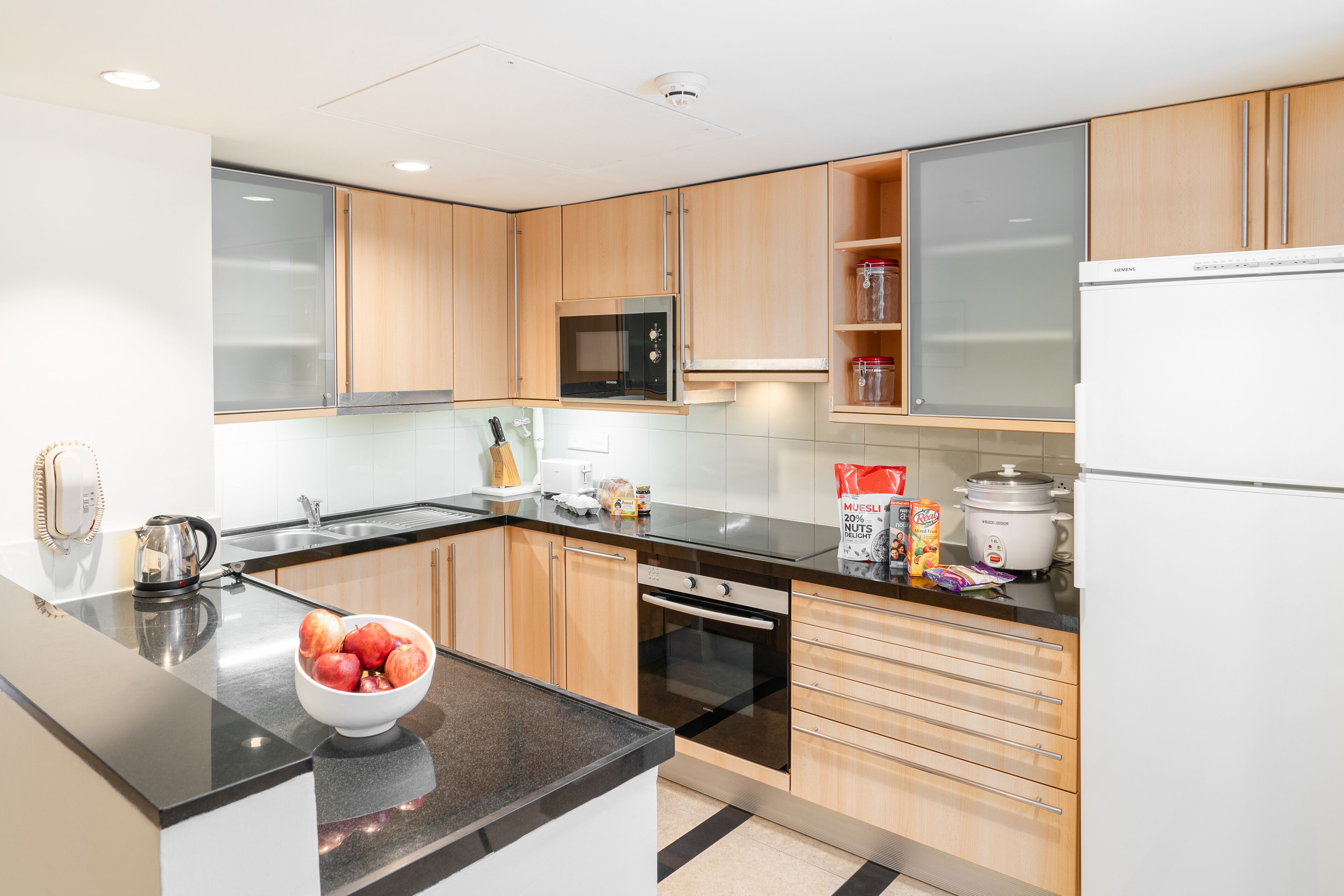 A modern kitchen with wooden cabinets, a black countertop, stainless steel appliances, and a bowl of fruit.