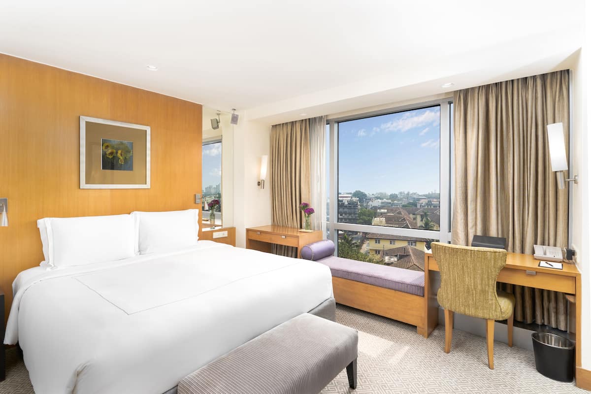 Habitación de hotel con una cama grande, un escritorio, una silla y vistas a la ciudad.