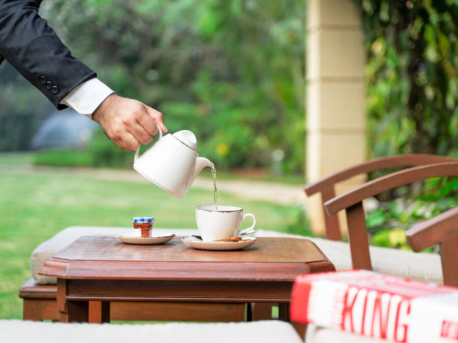 A hand pouring tea into a cup on a wooden table with a book titled "KING" beside it.