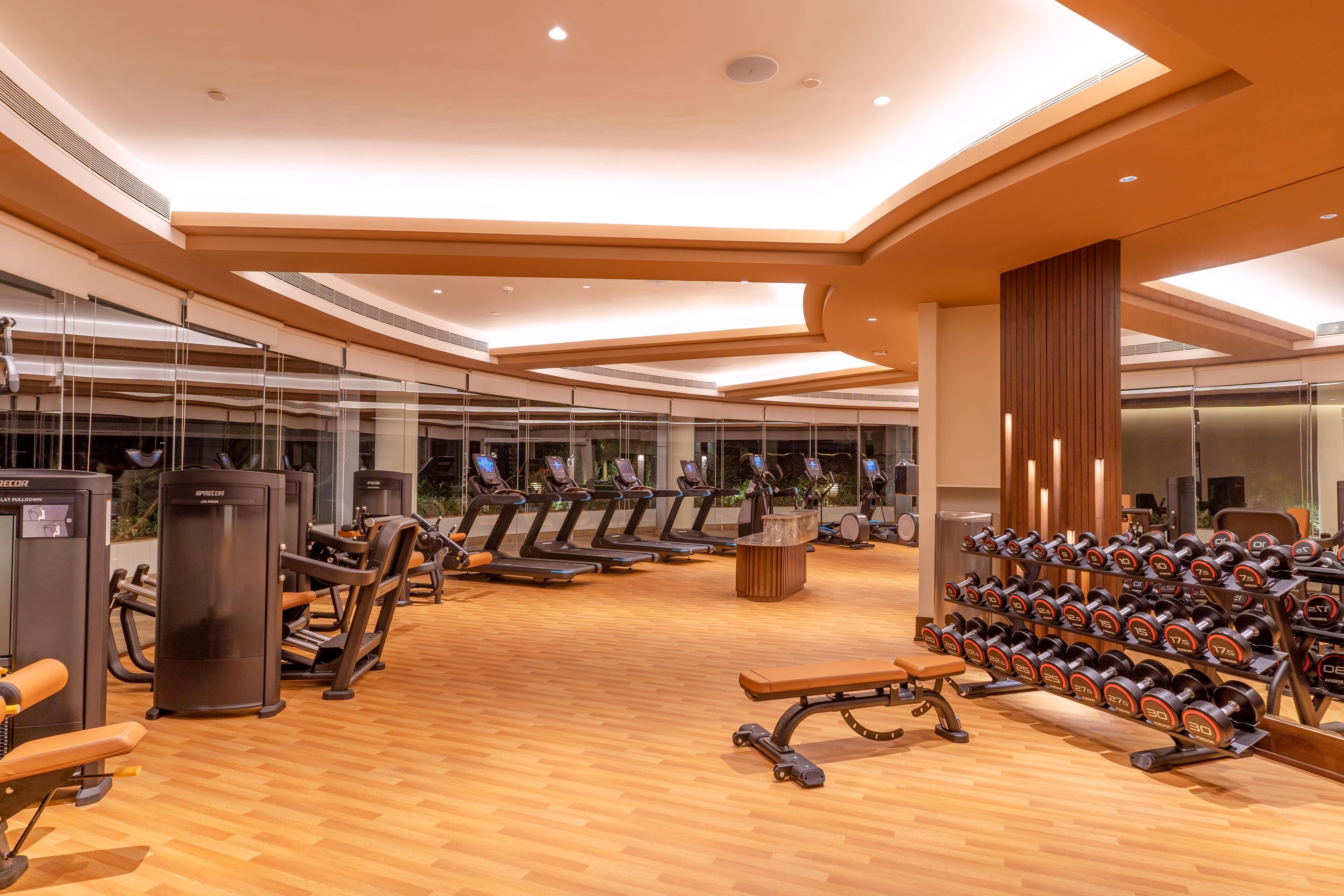 A modern gym with exercise equipment, mirrors, and a wooden floor.