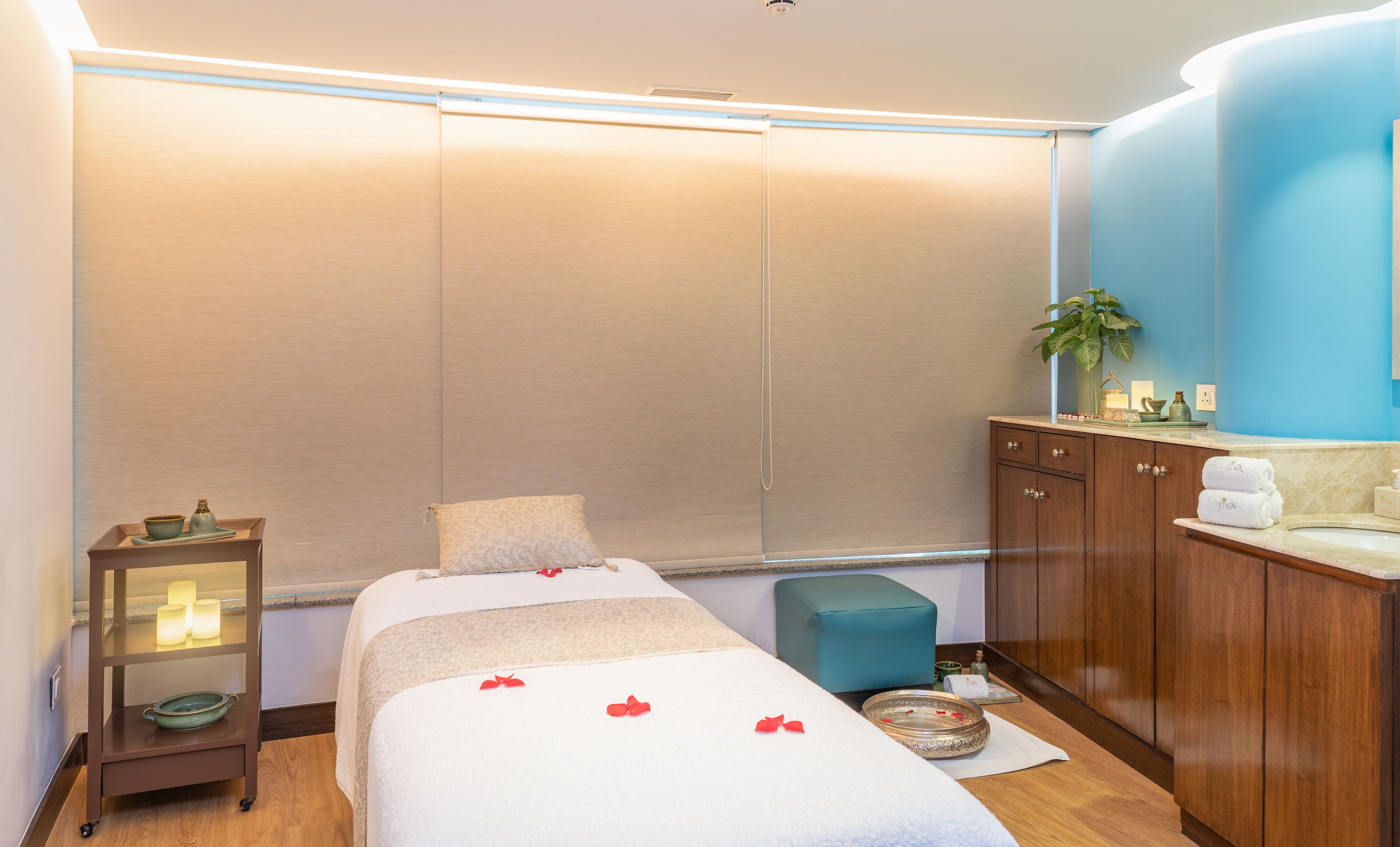 A spa room with a massage bed, a small table with candles, a cabinet with toiletries, and a blue wall.