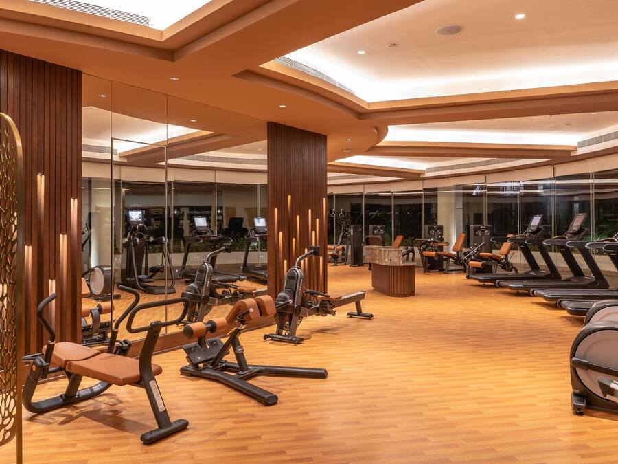 Een moderne sportschool met diverse cardio- en krachttrainingsapparatuur, grote spiegels en een houten vloer.
