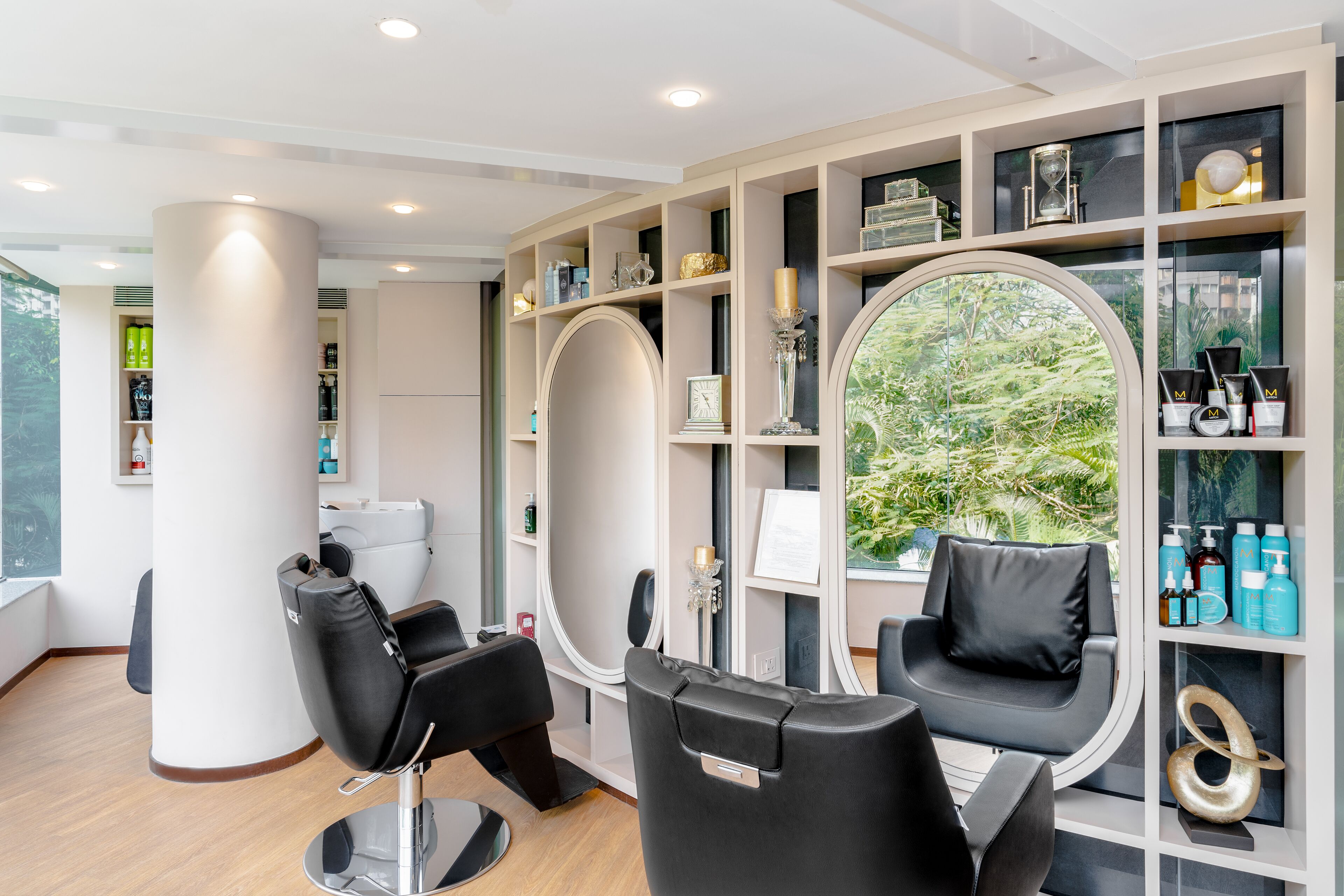 A modern salon with two black salon chairs, a large mirror, and shelves with hair products.