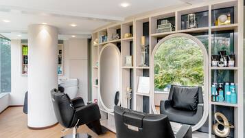 A modern salon with two black salon chairs, a large mirror, and shelves with hair products.