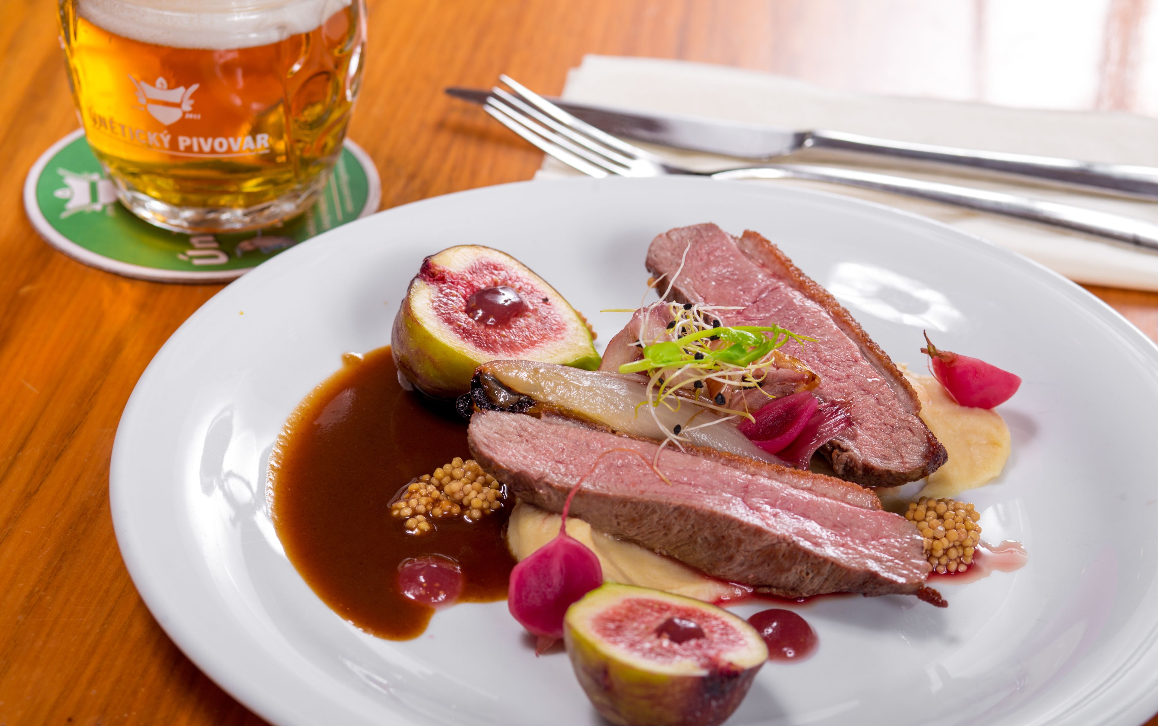 A plate of food with meat, fruit, and sauce, and a glass of beer on a coaster.