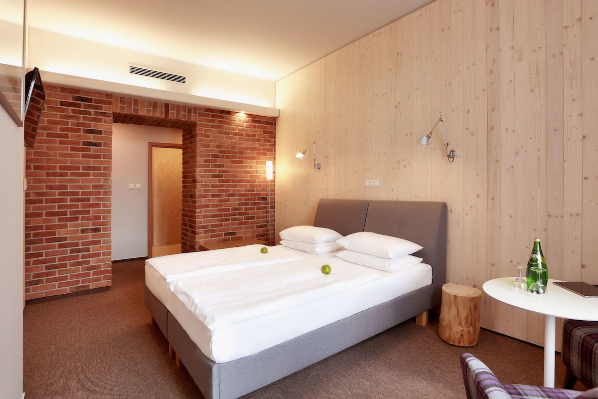 A hotel room with a large bed, a small table, and a wooden side table.
