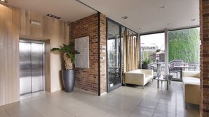 Un vestíbulo moderno con pared de ladrillo, una planta grande en maceta, un mostrador de recepción y una zona de estar con una mesa y sillas.