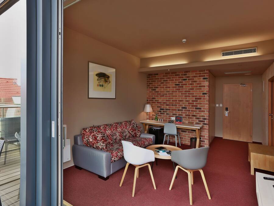A modern living room with a sofa, two chairs, a small table, a brick accent wall, and a door leading to another room.