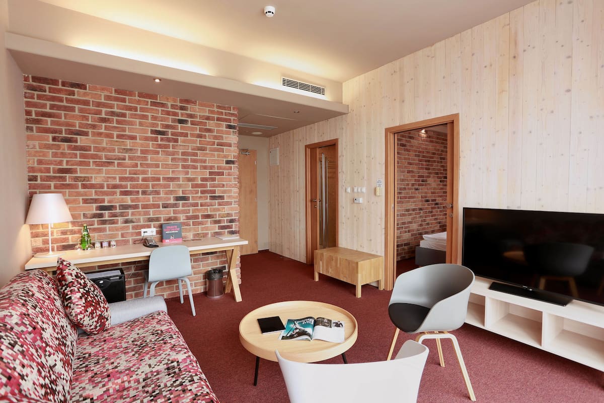 A modern living room with a brick wall, a flat-screen TV, a sofa, a coffee table, and a desk with a lamp.