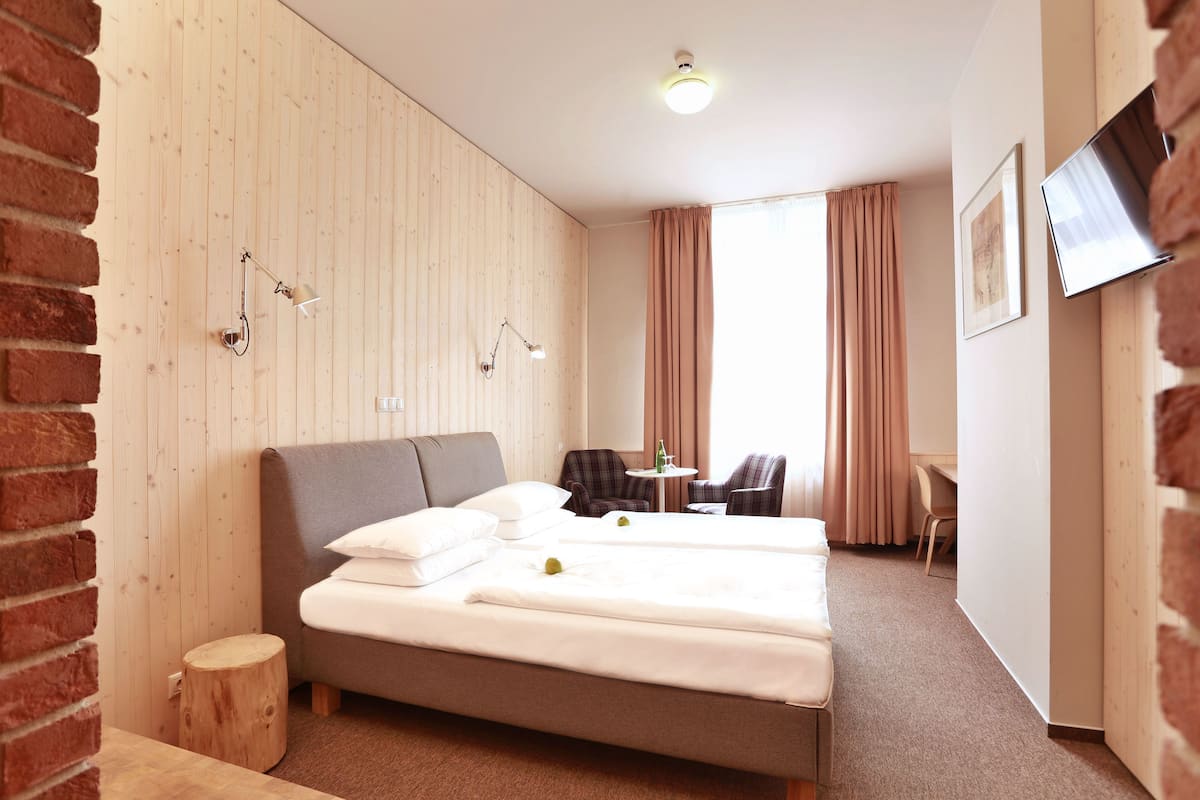 A hotel room with a large bed, two bedside tables, a small round table, a chair, and a TV mounted on the wall.