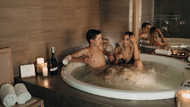 Un jacuzzi con tres personas, velas y una botella de vino sobre una encimera de madera.
