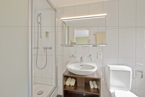 A modern bathroom with a glass shower enclosure, a white sink, and a toilet. - Sorell Hotel Asora (Arosa)