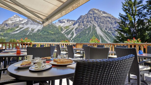 An outdoor dining area with tables and chairs, overlooking a mountainous landscape. - Sorell Hotel Asora (Arosa)