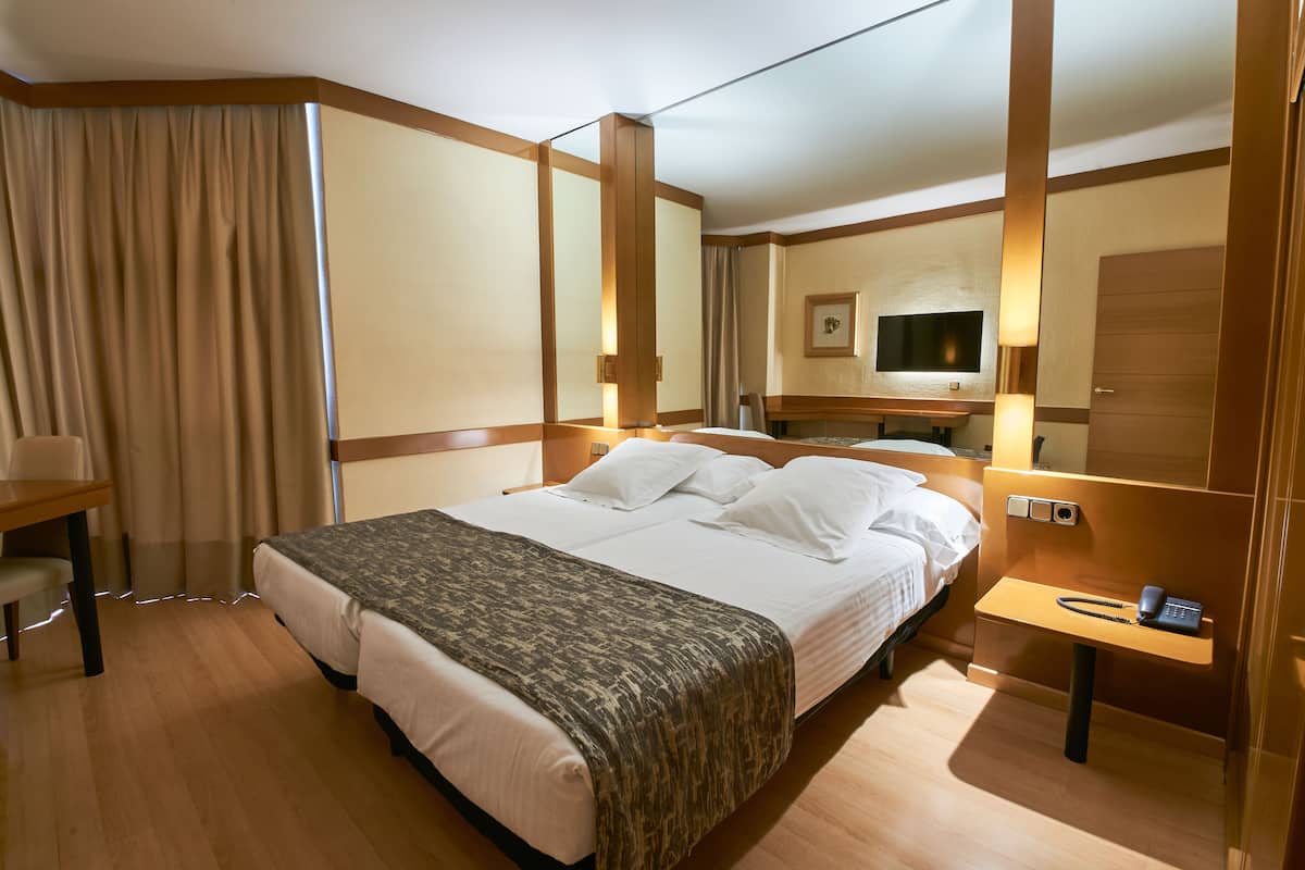 A hotel room with a large bed, a desk, a chair, a bedside table with a phone, and a TV mounted on the wall.