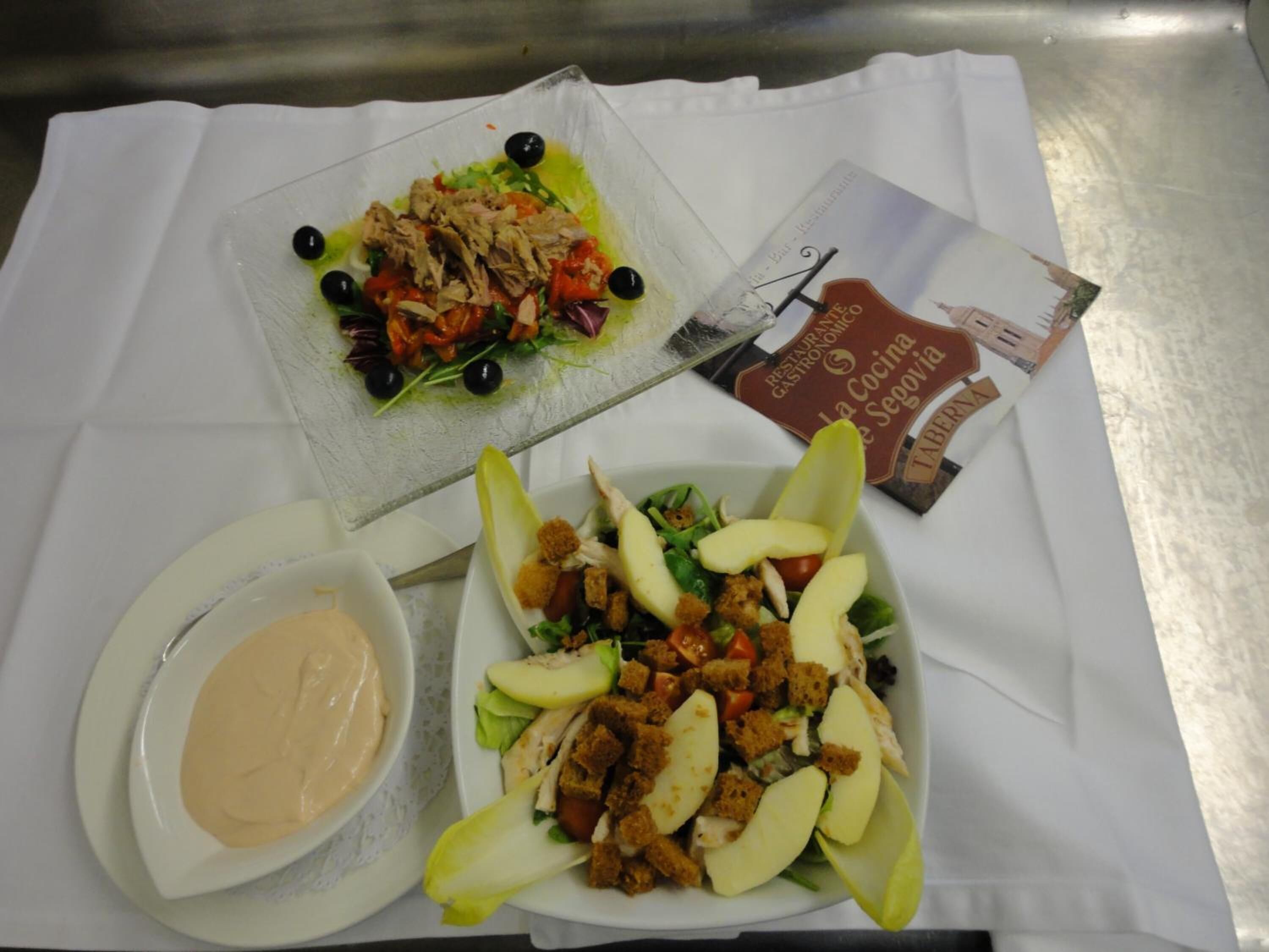 A table with two plates of food, a bowl of sauce, and a menu.