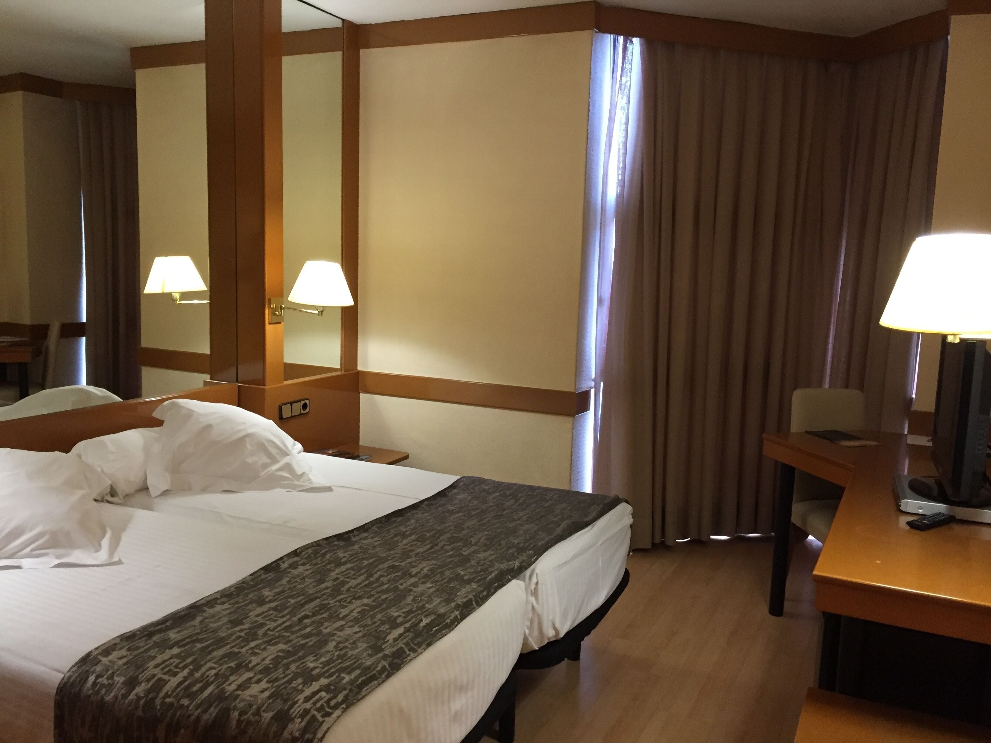 A hotel room with a large bed, a desk, a chair, a television, and a window with curtains.