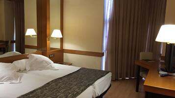 A hotel room with a large bed, a desk, a chair, a television, and a window with curtains.