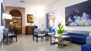 A modern living room with a blue sofa, two armchairs, a coffee table, and a large abstract painting. - Hotel AR Los Arcos (Segovia)