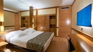 A hotel room with a large bed, wooden wardrobe, built-in desk, and a flat-screen TV mounted on the wall. - Hotel AR Los Arcos (Segovia)