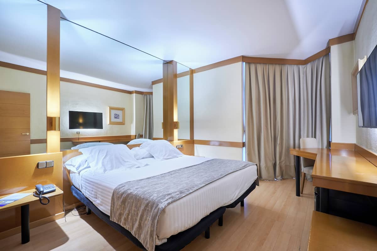 A hotel room with a bed, bedside table, lamp, and a large mirror.