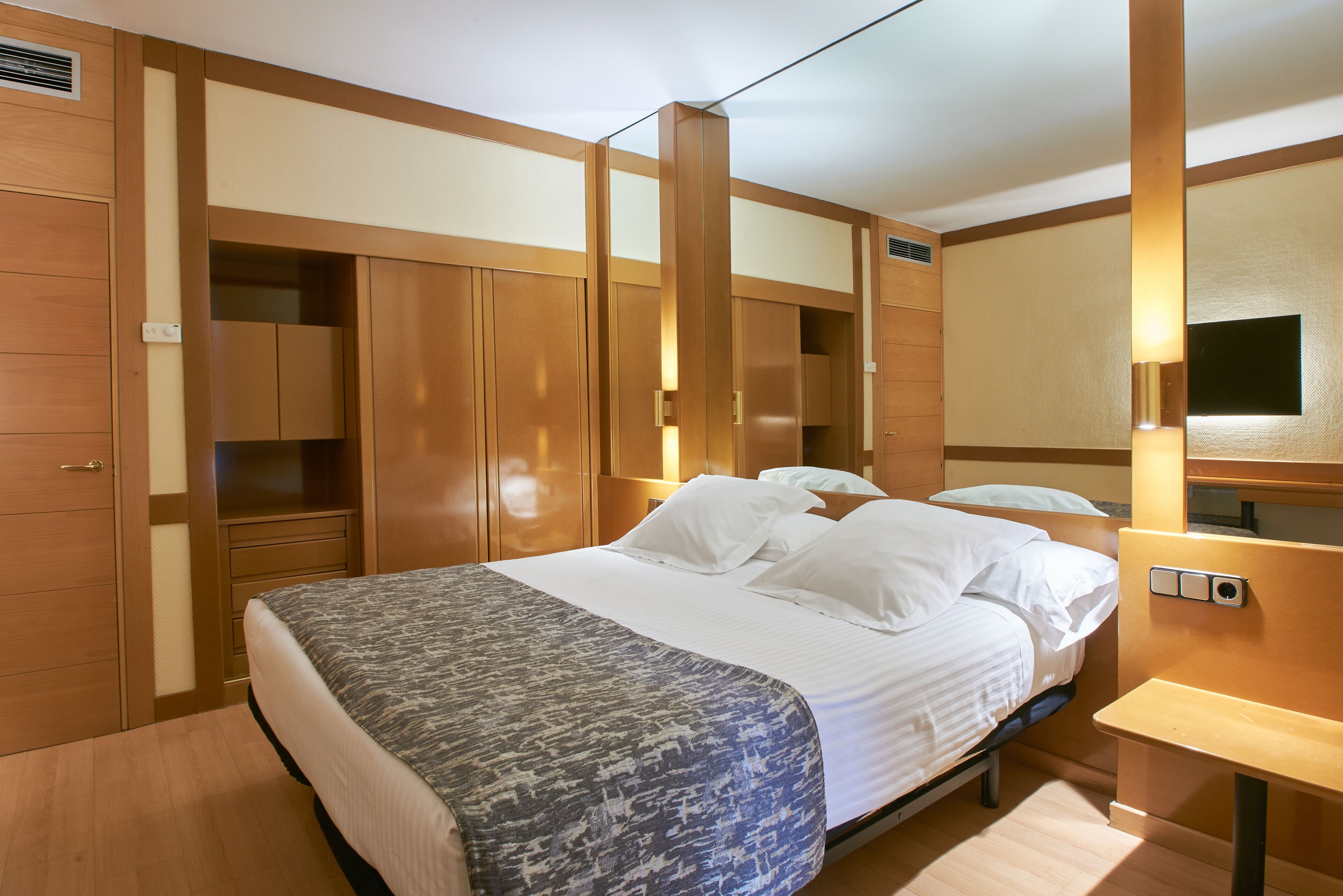 Una habitación de hotel con una cama grande, un armario de madera y una mesita de noche.