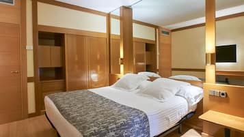 A hotel room with a large bed, wooden wardrobe, and a bedside table.