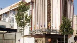 A hotel with a prominent "Hotel" sign, a large entrance with a canopy, and multiple flags displayed outside. - Hotel AR Los Arcos (Segovia)