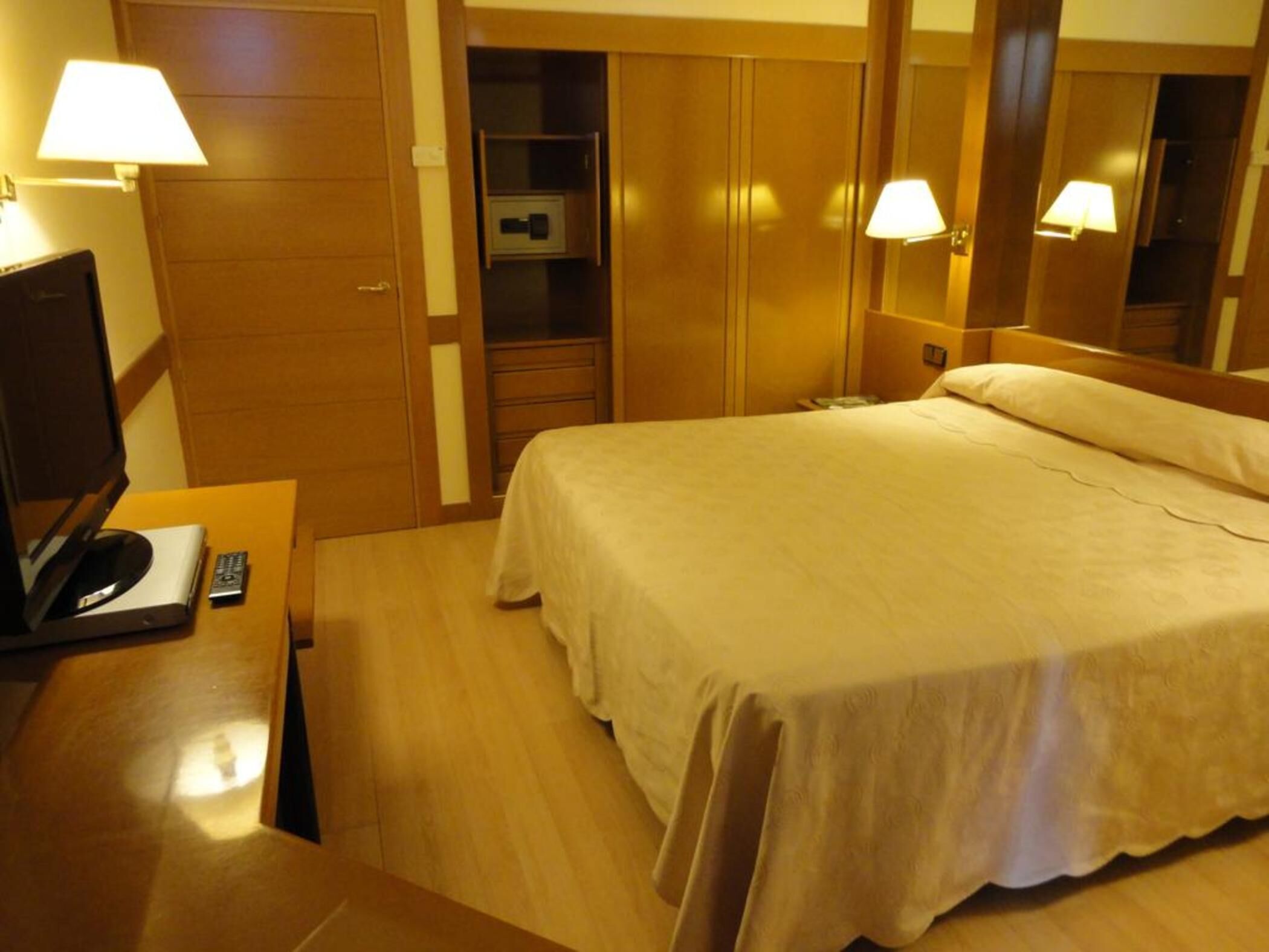 A hotel room with a bed, a desk with a lamp, a television, and a wardrobe.