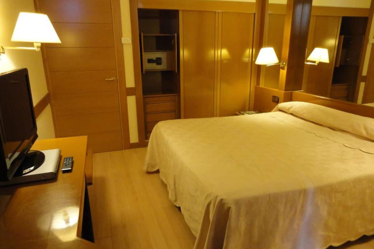 A hotel room with a bed, a desk with a lamp, a television, and a wardrobe.