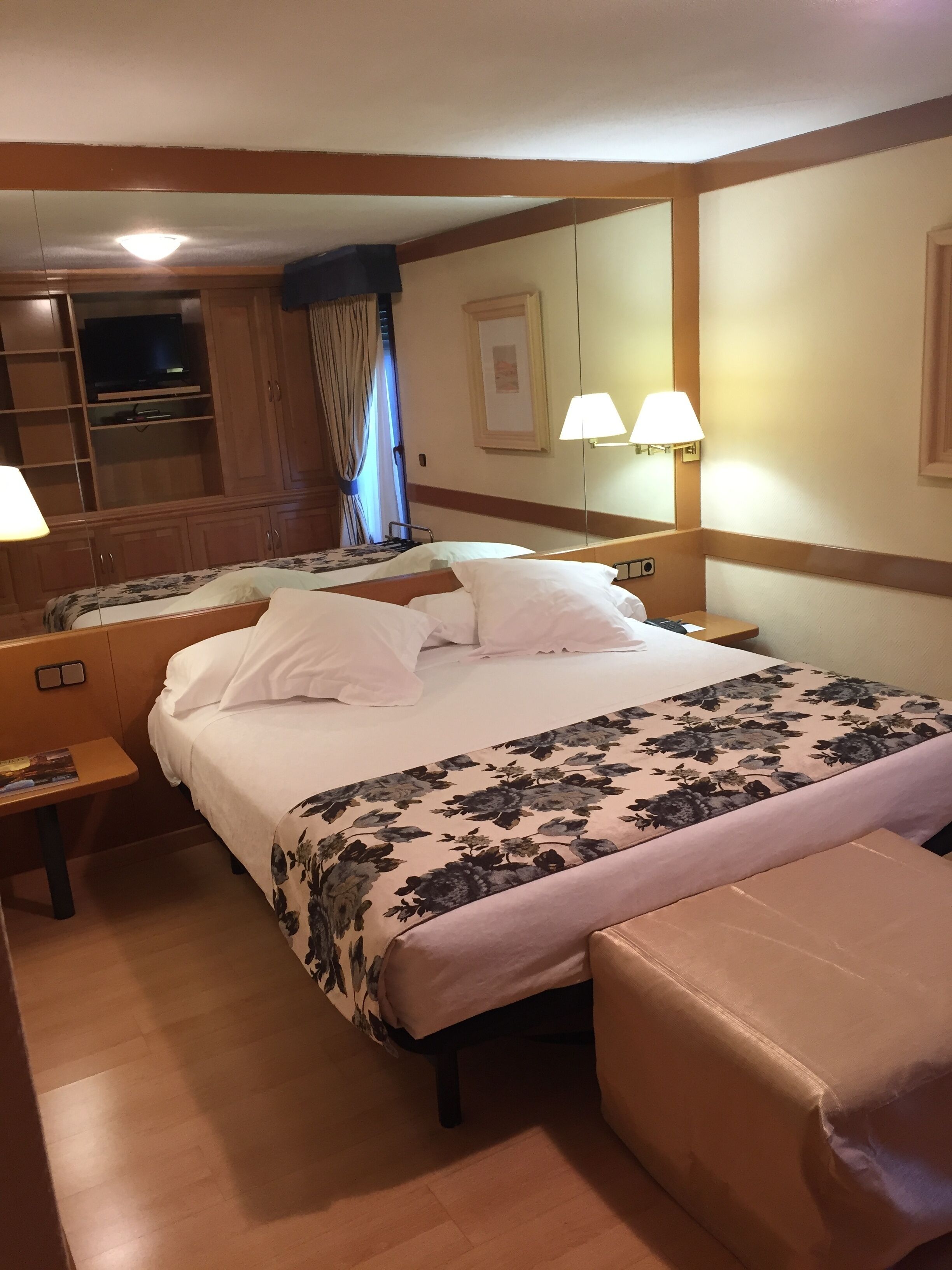 A hotel room with a large bed, a bedside table, a nightstand, a mirror, and a wardrobe.