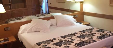 Una habitación de hotel con una cama grande, una mesita de noche, un armario y un espejo.