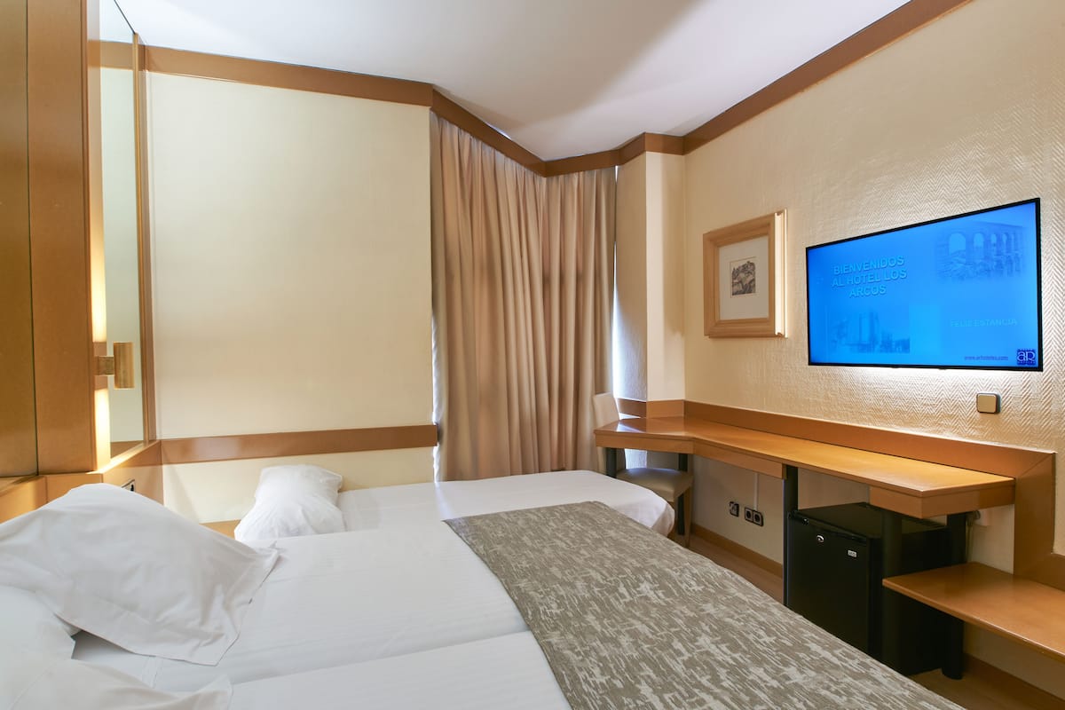 A hotel room with a bed, a desk, a television, and a small refrigerator.