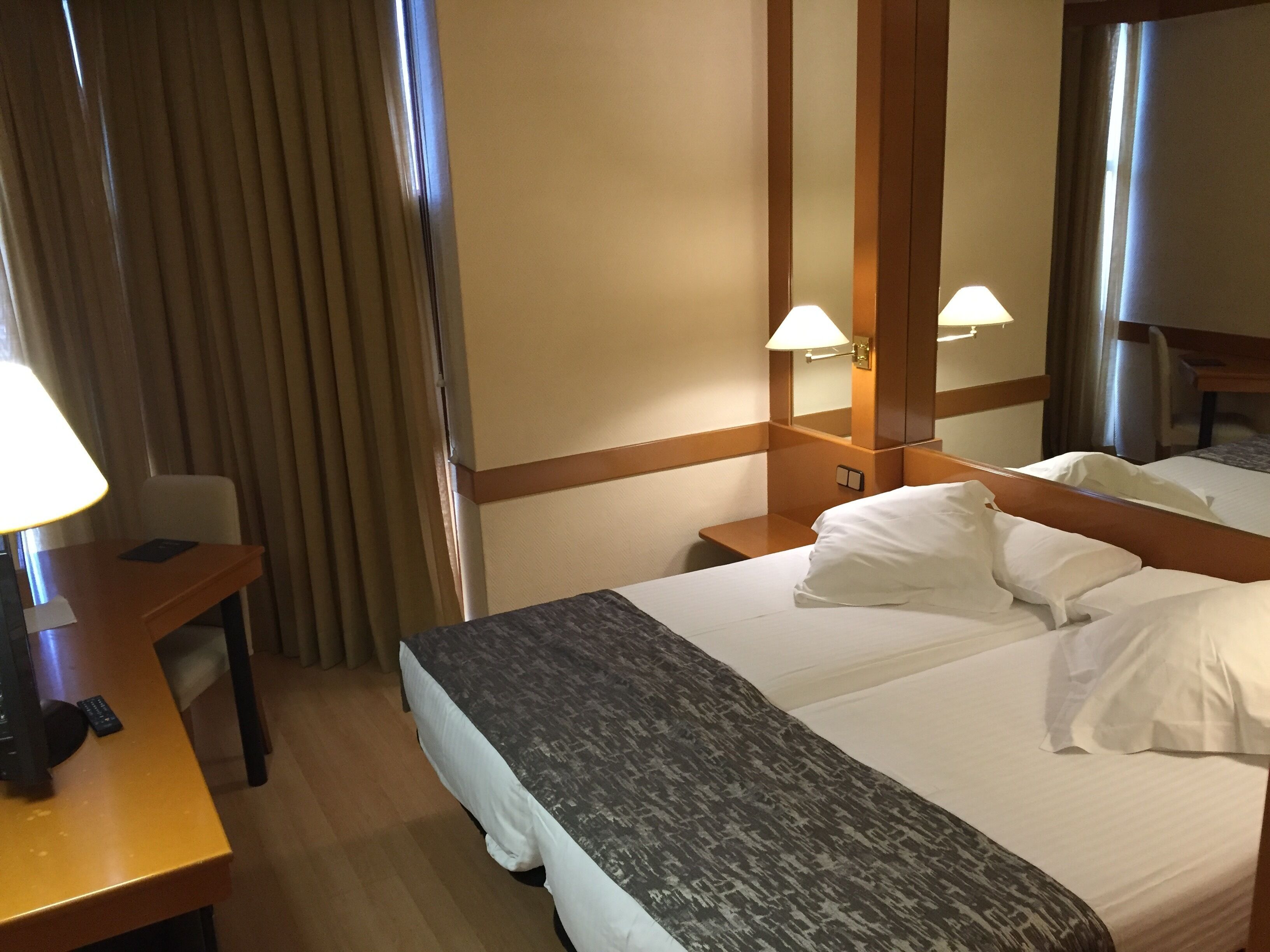 A hotel room with a bed, bedside table, lamp, and a mirror.
