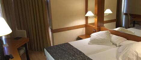 Una habitación de hotel con cama, mesita de noche, lámpara y espejo.