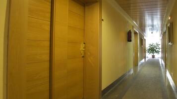 Un pasillo con puertas de madera, suelo de baldosas y techo con diseño de cuadrícula.