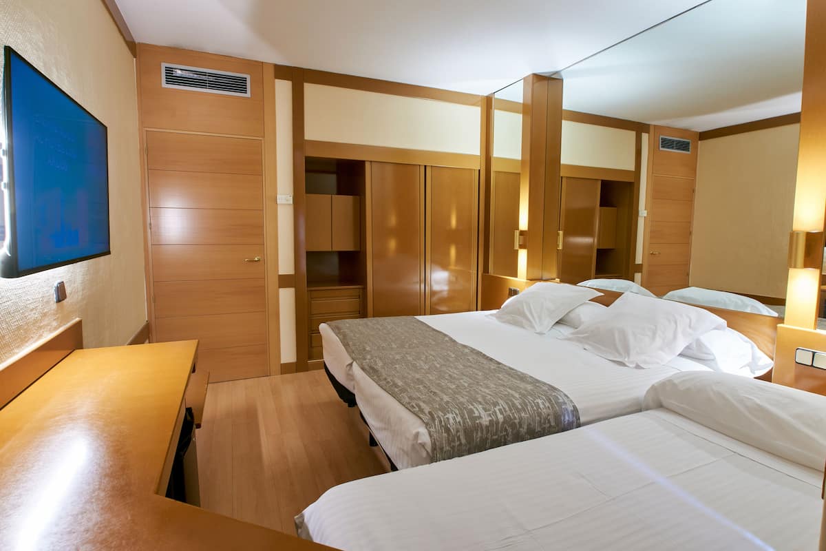 A hotel room with two beds, wooden furniture, a TV mounted on the wall, and built-in wardrobes.