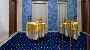 A hotel room with a blue carpet, a table with a yellow tablecloth, and a mirror reflecting the room. - HD Hotel (Milan)